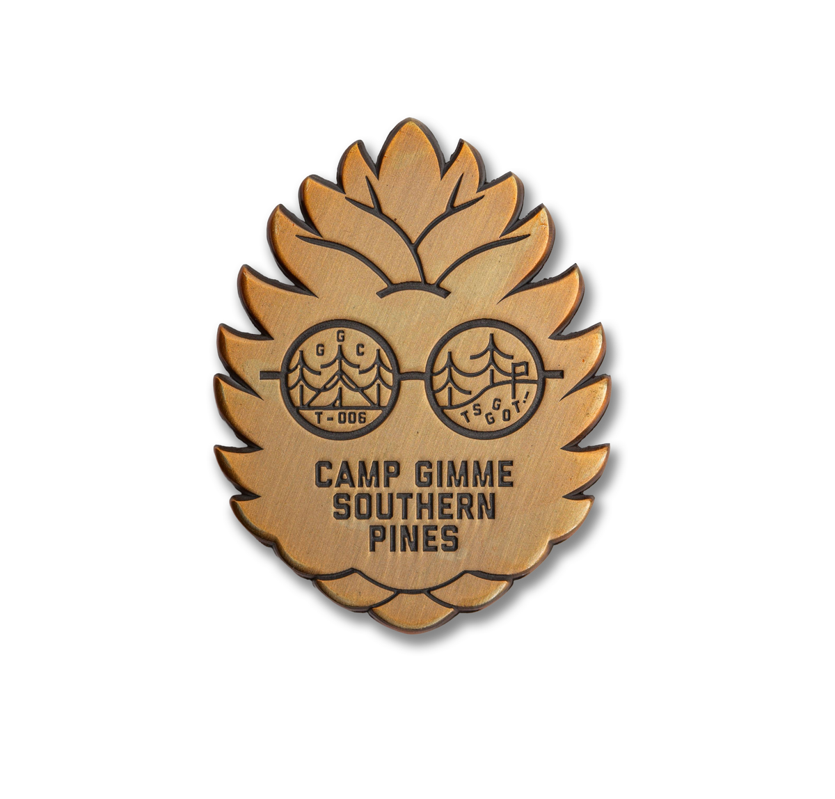 Metal badge with 'Camp Gimme Southern Pines' text and pine cone design on a white background